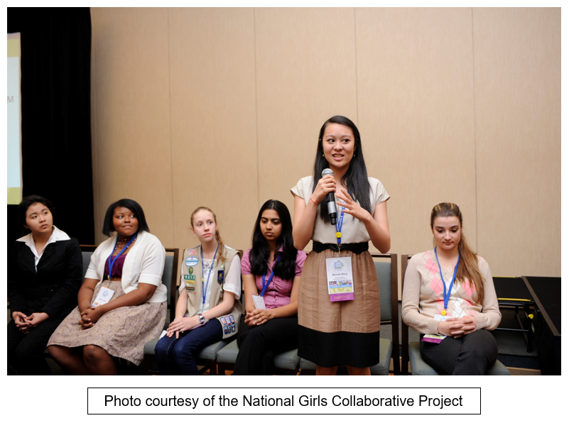 A girl speaks into a microphone while other girls look on. Text reads: 
Photo courtesy of the National Girls Collaborative project."